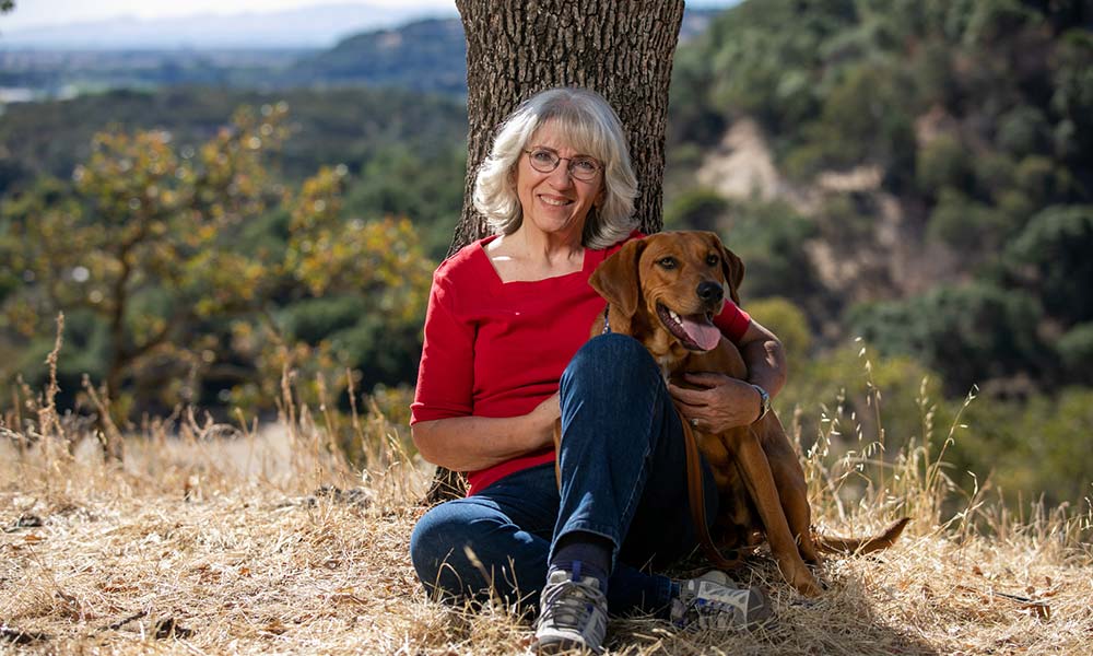 Sally sitting with a dog on a hillside overlooking a valley