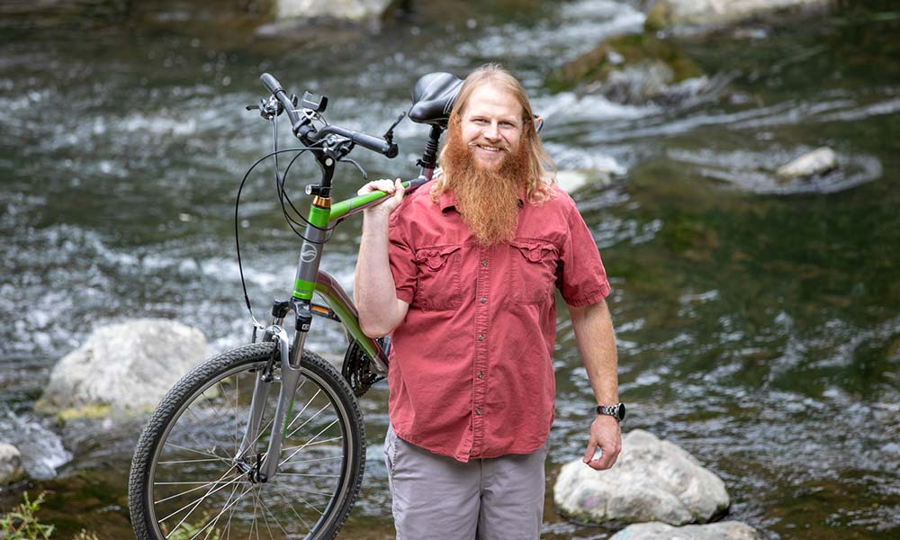 Steve standing in front of a stream of water, carrying a bike